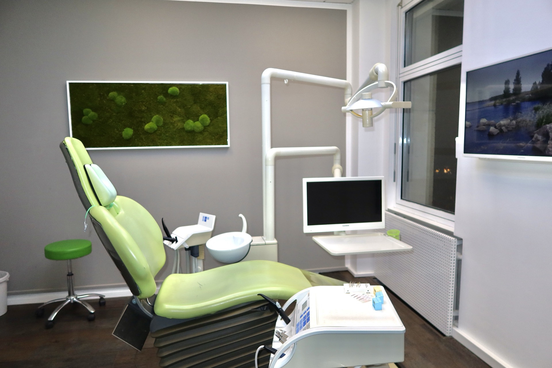 Moderner Behandlungsraum mit grünem Behandlungsstuhl, Moosbild und Naturmotiv bei Dr. Pantas Düsseldorf