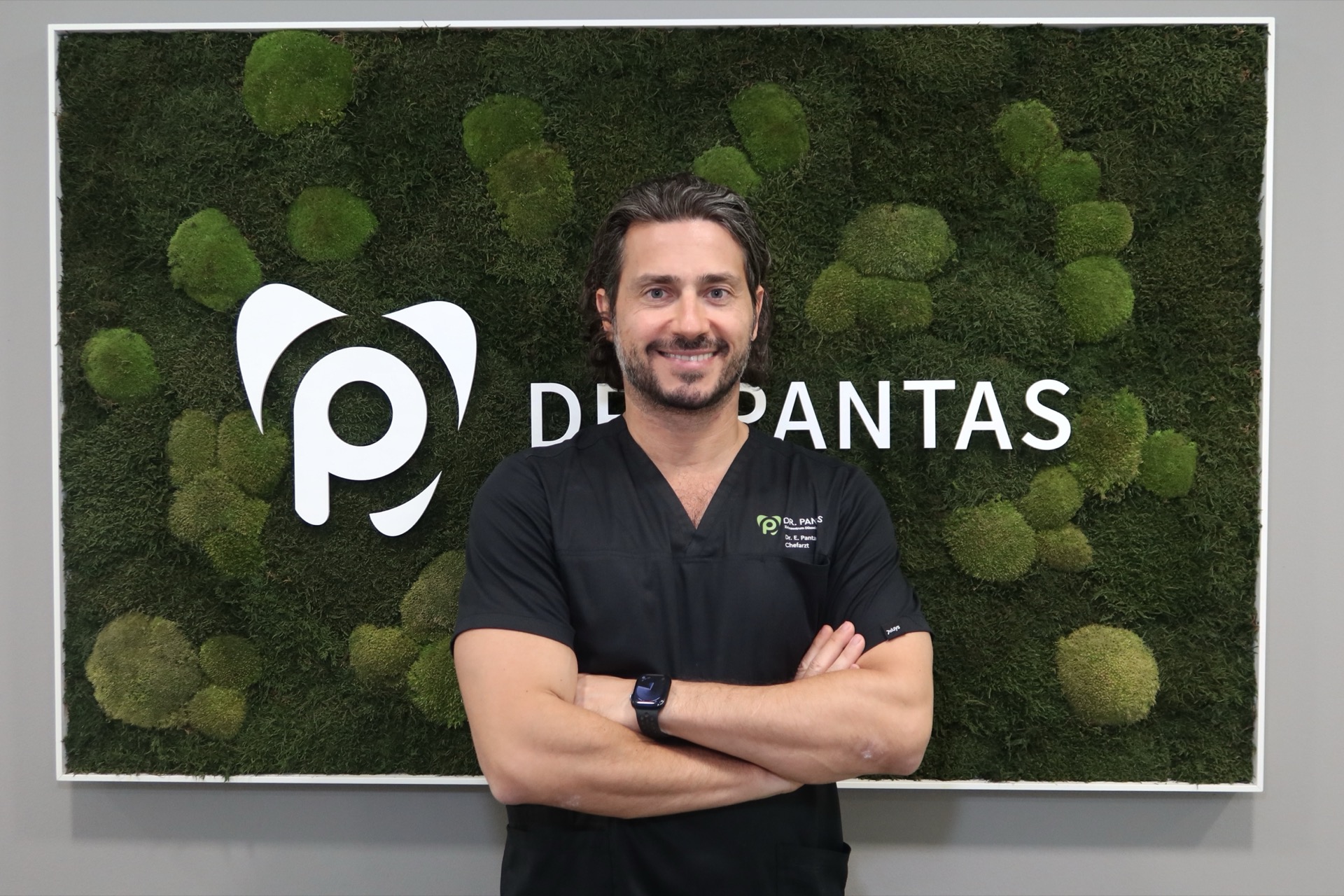 Dr. Pantas vor der Praxis-Logowand mit Moosbild — Zahnzentrum Düsseldorf